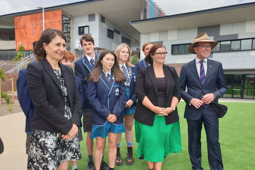 Three politicians smiling with school students at a public school opening.