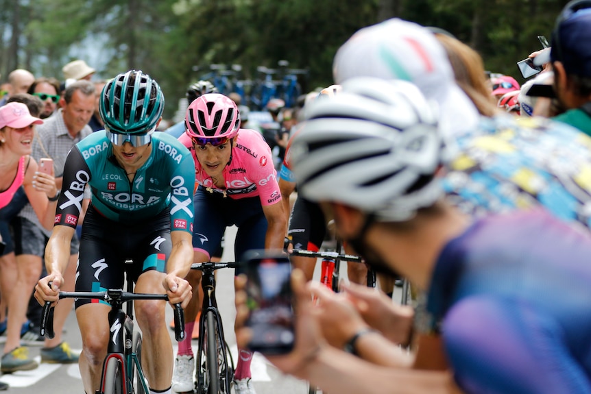 Jai Hindley lidera a RIchard Carapaz con una multitud alrededor de la carretera frente a ellos