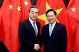 Chinese Foreign Minister Wang Yi and Vietnamese Foreign Minister Pham Binh Minh shake hands in front of red flags.
