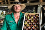 A close up of farmer Ash Emerick in a green shirt and cream hat, holding a box of figs.