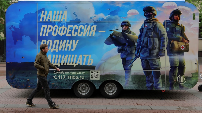 A pedestrian walks past a mobile recruitment point with soldiers painted on the side. 