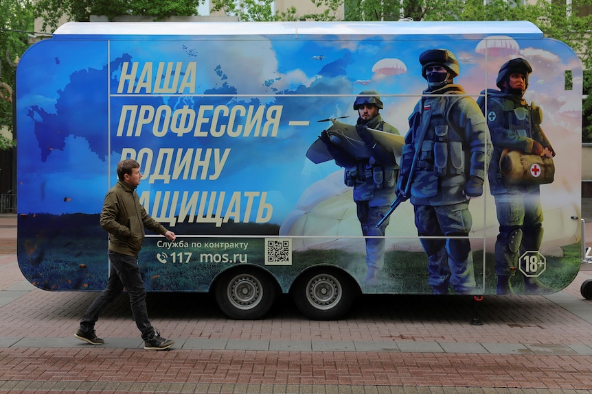 A pedestrian walks past a mobile recruitment point with soldiers painted on the side. 