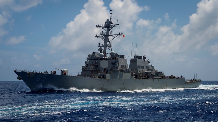 A grey warship travels through blue waters on a sunny day.