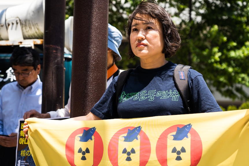 An Asian woman holding a yellow banner stares straight ahead.