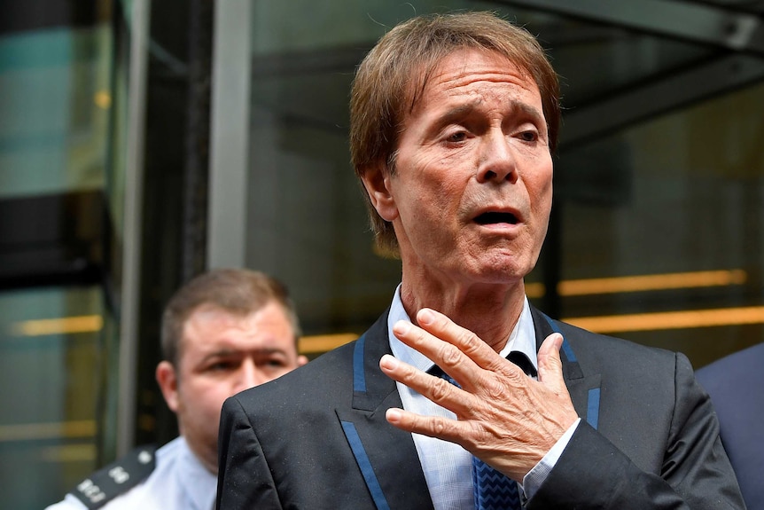 Singer Cliff Richard leaves the High Court with his hand held before his chest in an emotional gesture.