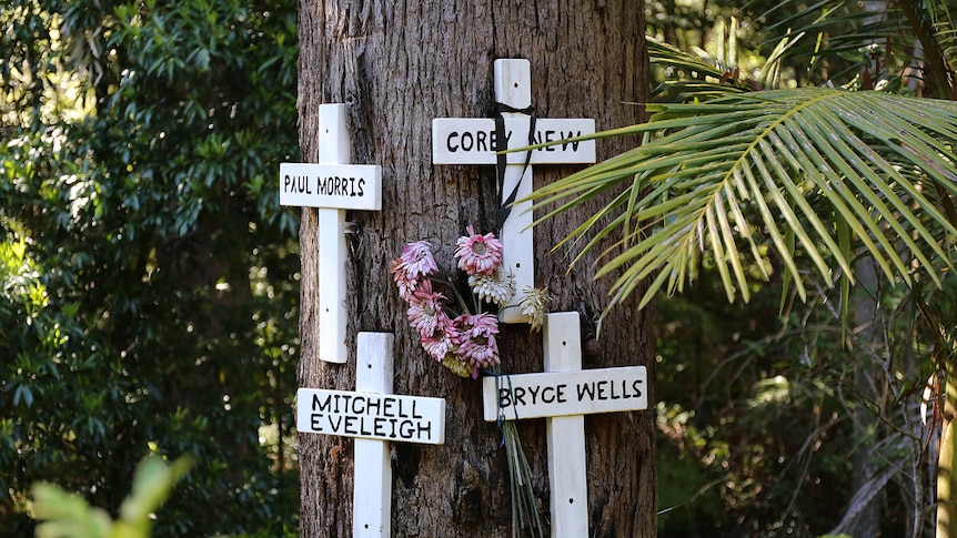 A tree trunk with four white crosses nailed to it, and a bunch of drooping flowers.