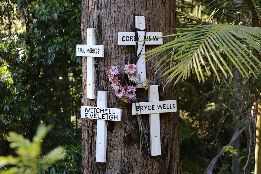 A tree trunk with four white crosses nailed to it, and a bunch of drooping flowers.