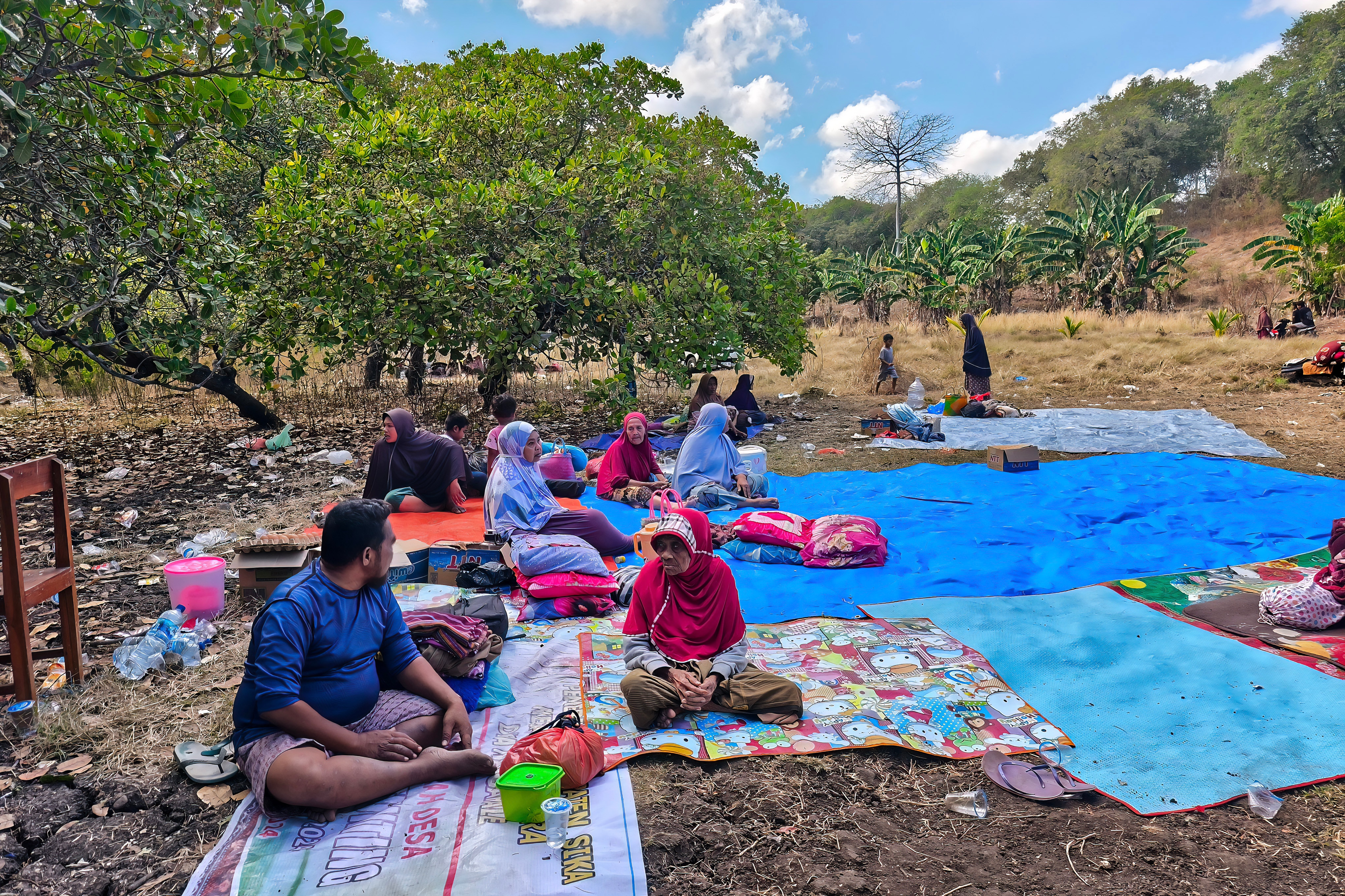 A group of people sit on blanket and tarpulins in a field.