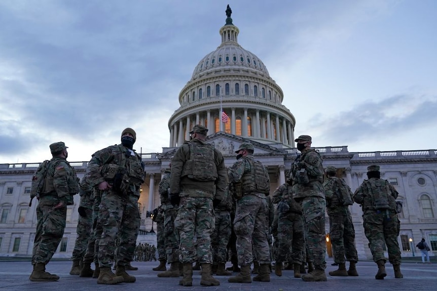 People in army fatigues stand in front of the US Capitol building