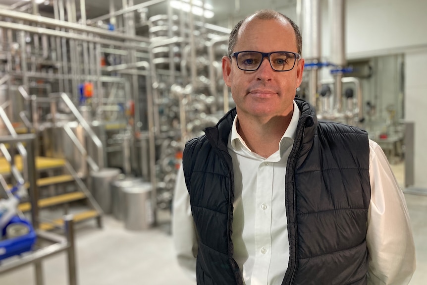 A man in white shirt and black vest stands in a factory.