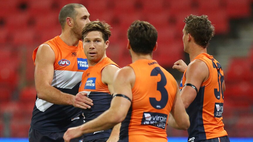 A group of AFL teammates gather around a player after he kicks a goal.