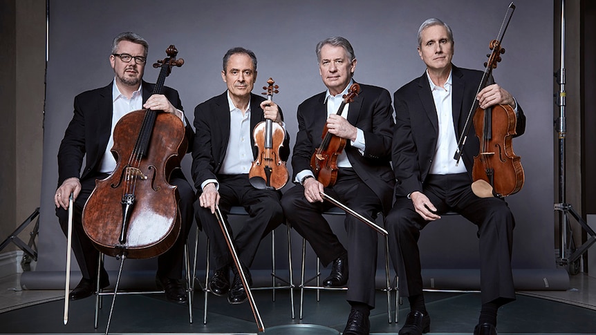 There Emerson String Quartet pose with their instruments in a photo studio.