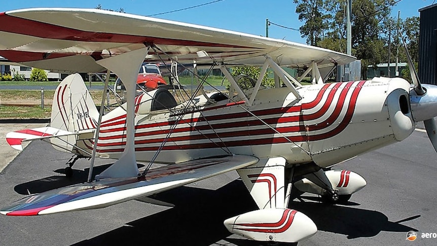 A white bi-plane with red stripes along the side of the fuselage and wheel covers.