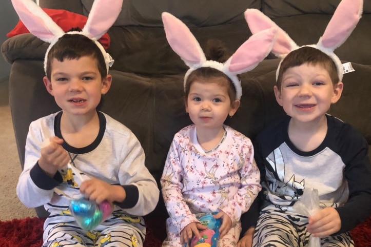 Little girl on floor seated between brothers, all wearing bunny ears.
