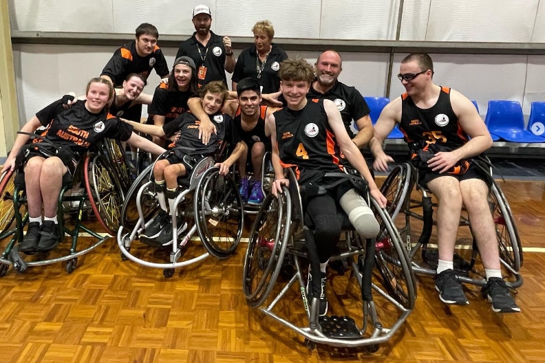A wheelchair basketball team smiles and poses for the camera.