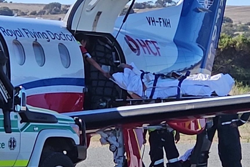 A person strapped on to a stretcher being lifted into a small medical plane