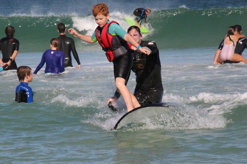 A boy surfs a wave with an instructor helping him.
