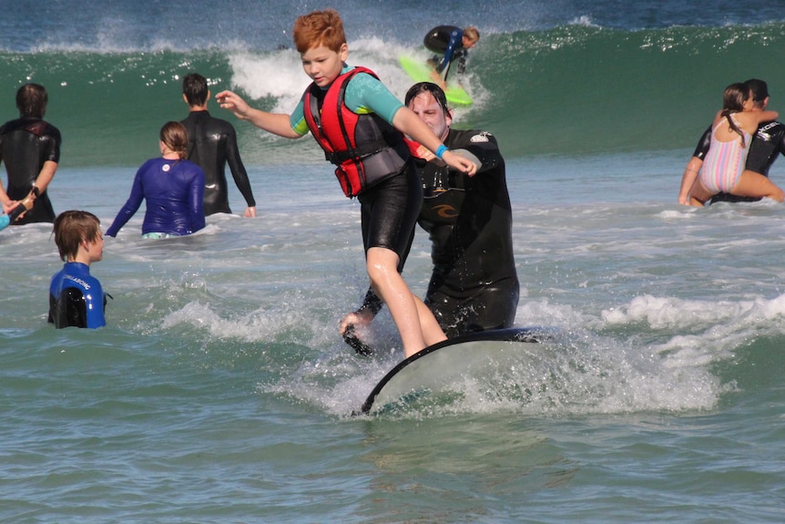 A boy surfs a wave with an instructor helping him.