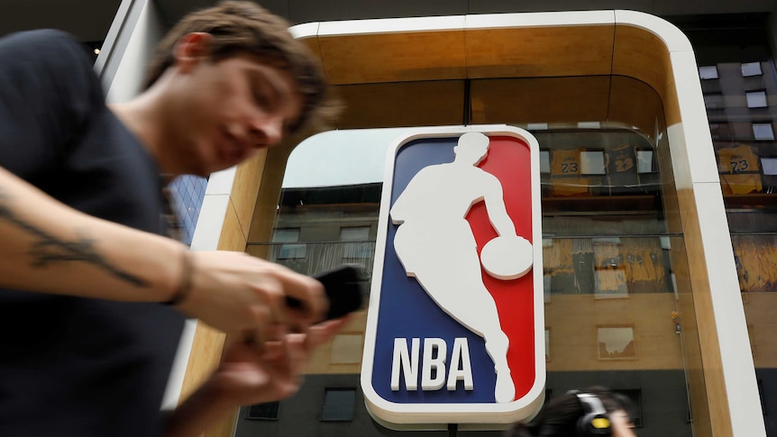 A man walks by a store, displaying the logo of the NBA basketball league.