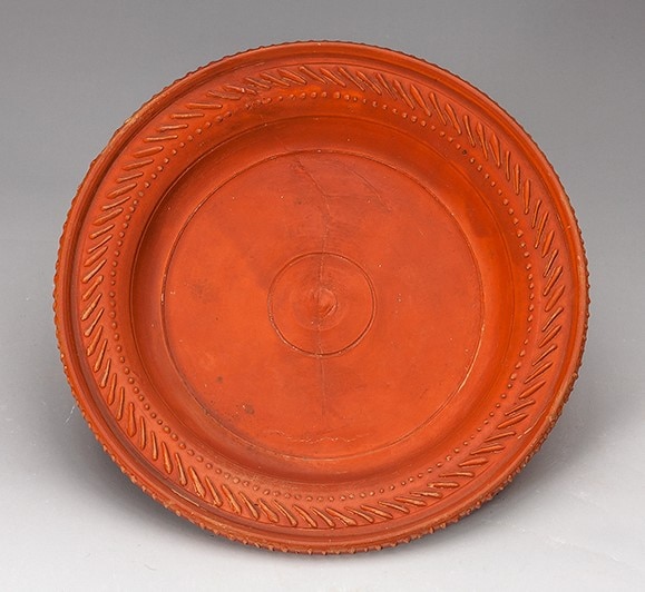 A handmade plate with a warm red slip and line detailing around the edge.