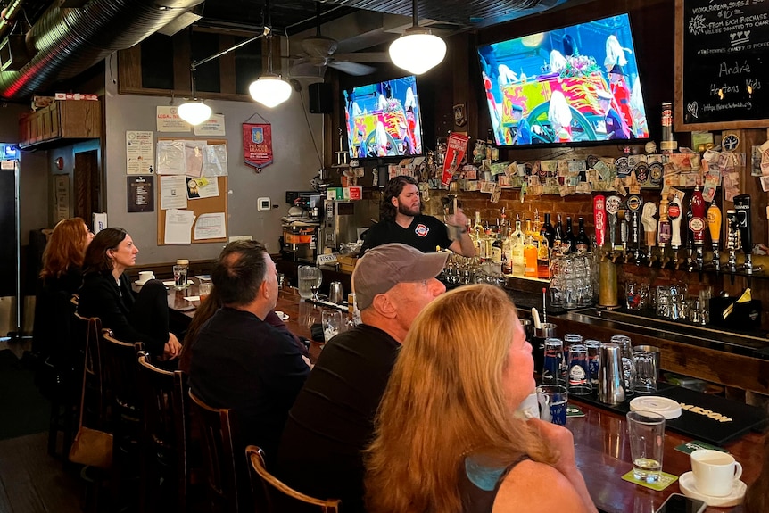 El funeral de la reina se transmite por televisión y la gente lo ve desde el bar. 