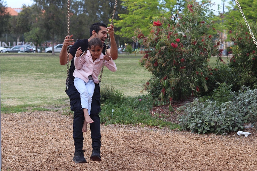 A man and his daughter play on the swings, big smiles