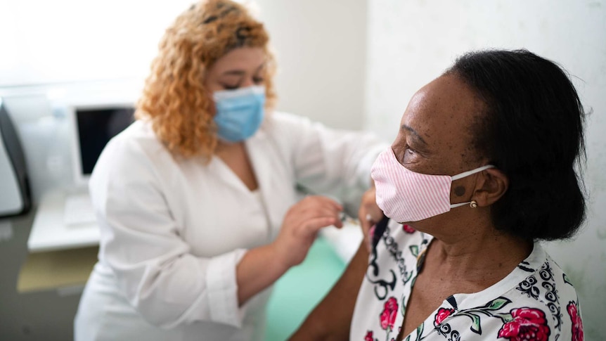 Nurse applying vaccine on patient's arm using face mask.