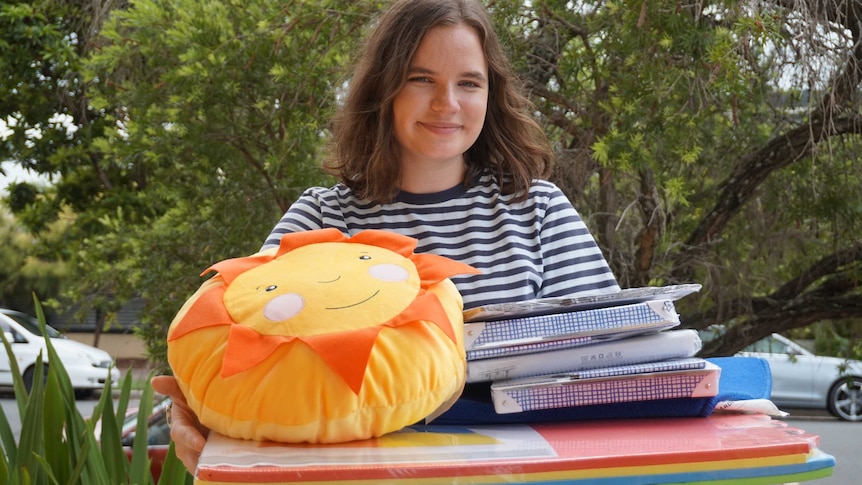 Ellen Wengert, wearing a black and white striped shirt, holds folders and a sunflower cushion.