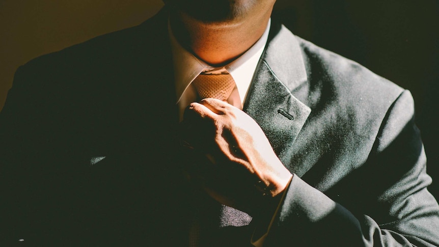 A man in a black suit adjusts his tie.