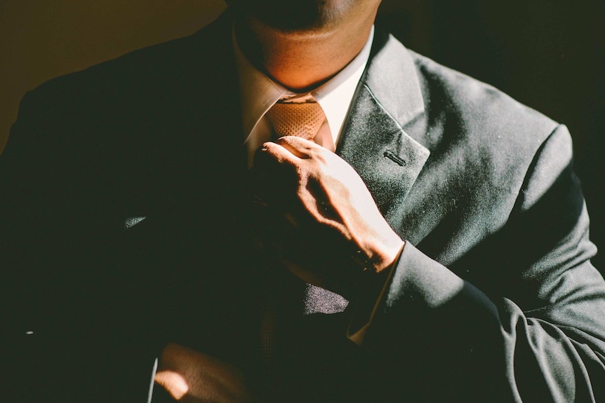 A man in a black suit adjusts his tie.