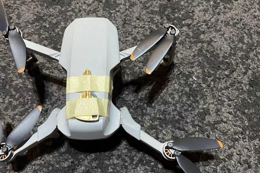 A gold key taped tightly to the top of a grey drone.