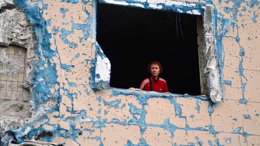 A woman looks out from a destroyed window of a residential building bombed by Russian forces in Kyiv, Ukraine.