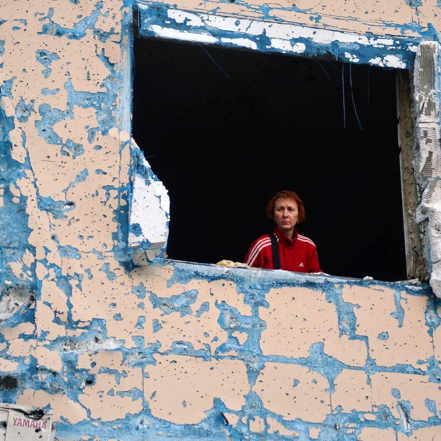 A woman looks out from a destroyed window of a residential building bombed by Russian forces in Kyiv, Ukraine.