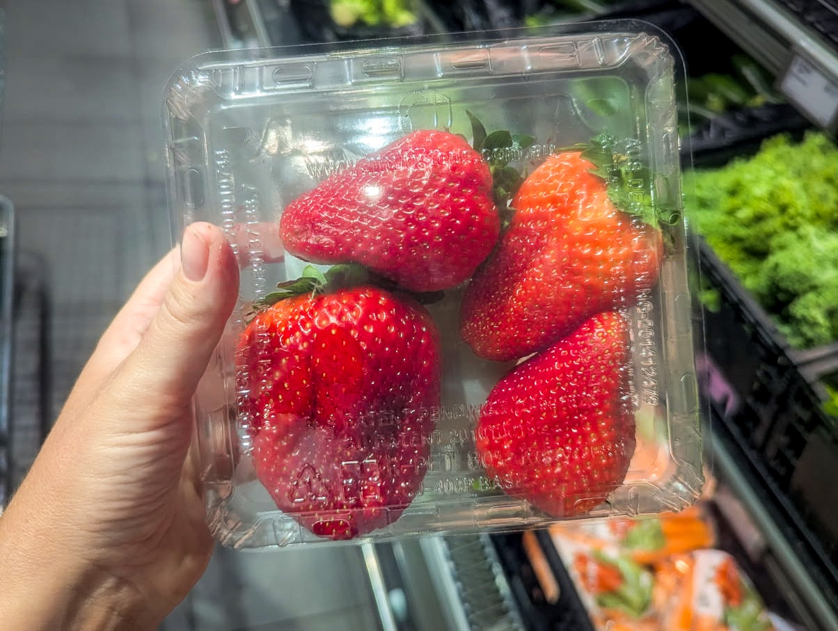 Quatro morangos grandes enchem uma cesta de plástico. 