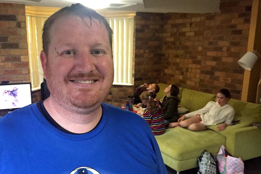 Larry Emery at home with his children on the lounge, out of focus, in the background.