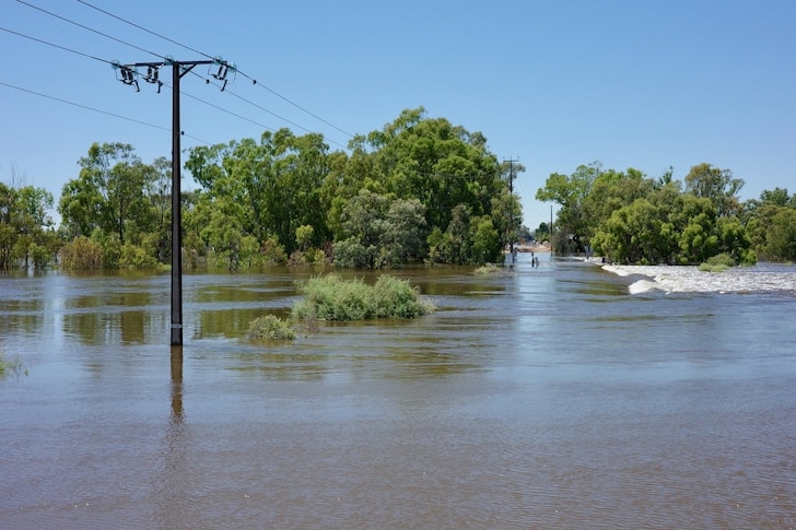 A power pole sticking up through floodwater beneath a clear sky.