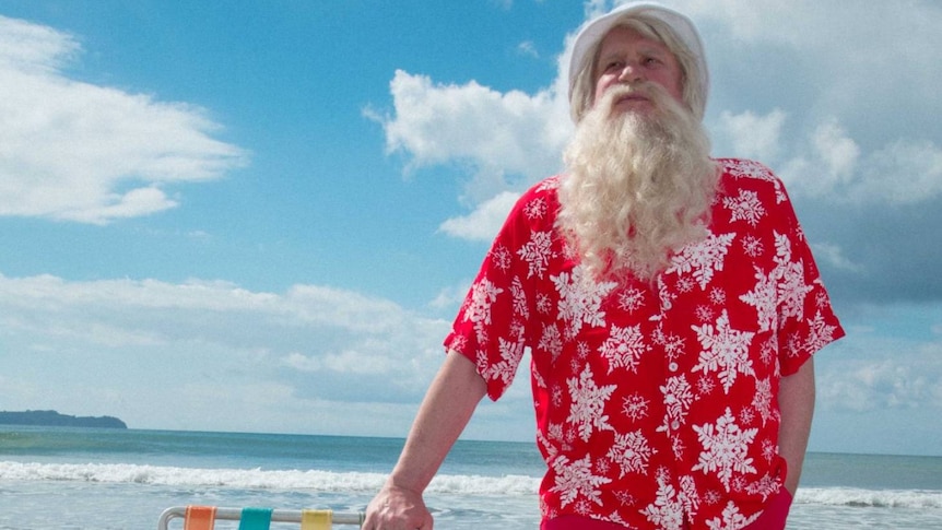 Santa in a hawaiian style red shirt, on the beach.
