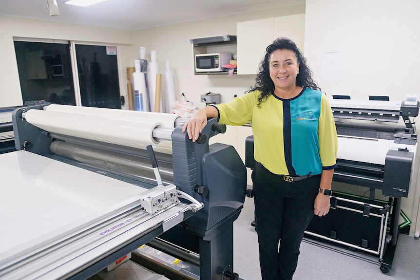 Donna-Marie Grieve stands in a green and blue shirt in a printing office.