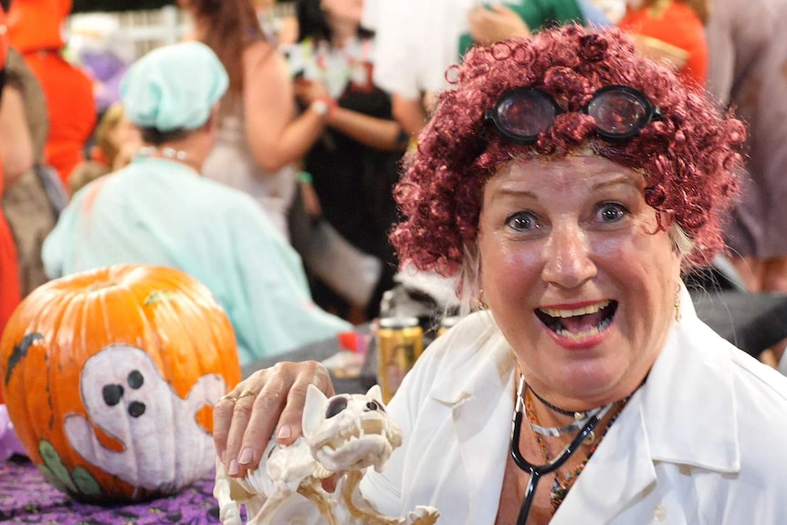A woman dressed as a mad doctor holds up the skeleton of  cat