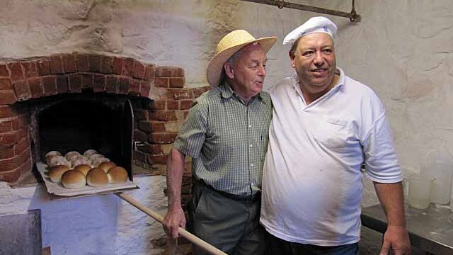 Two men at an old bakery, with buns nearby.
