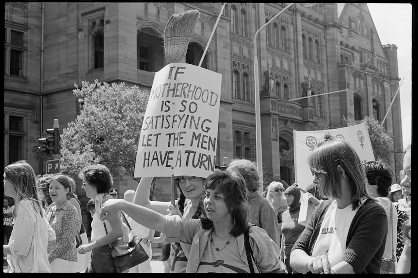 A black and white image of street protesters with a sign "if motherhood is so satisfying' let the men have a turn"