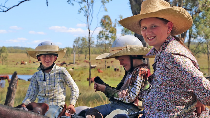 A girl and two boys sitting on their horses wearing cowboy hats and smiling