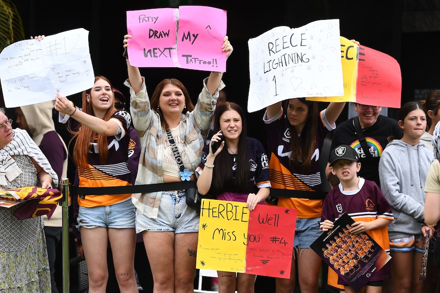 a crowd of fans with homemade signs supporting their favourite Brisbane Broncos players