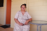 A woman sits at a small round table in front of a brick motel room.