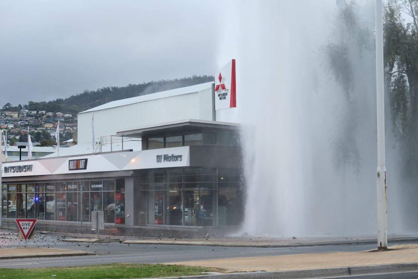 Debris strewn around the site of a  burst water main in Hobart as water spouts into the air.