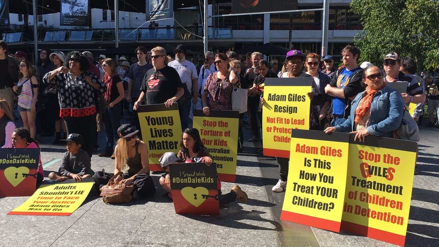 A crowd of people hold signs criticising NT Chief Minister Adam Giles.