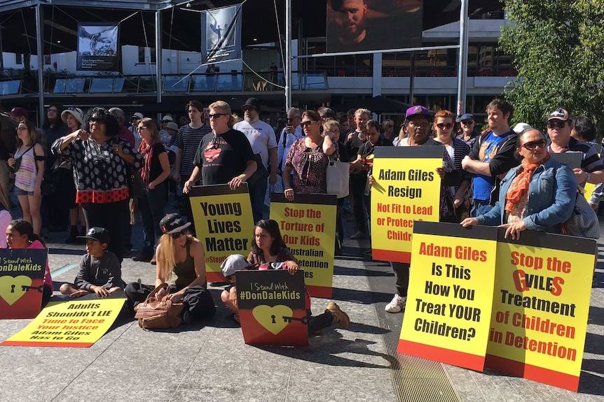 A crowd of people hold signs criticising NT Chief Minister Adam Giles.