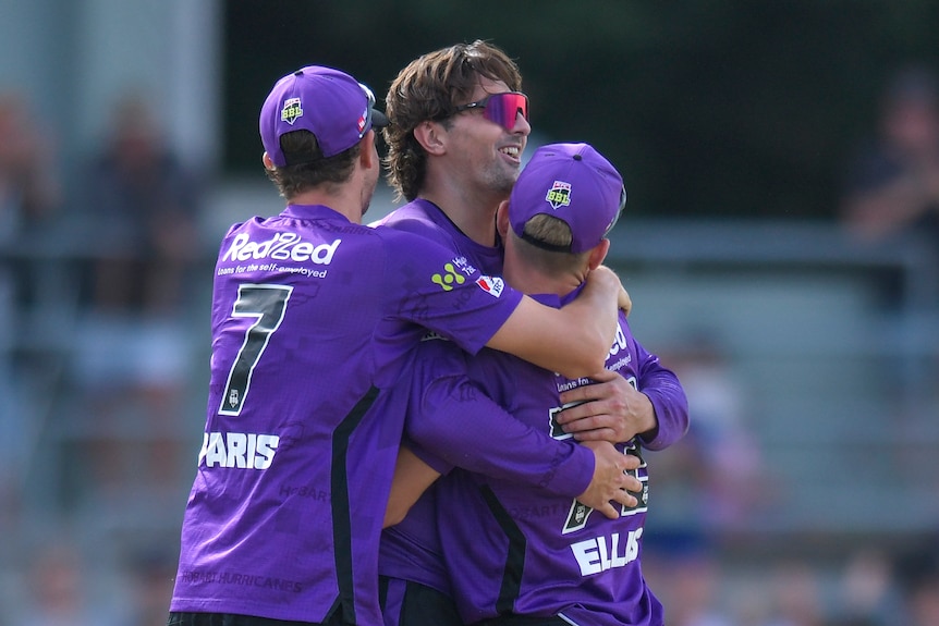 A trio of Hobart Hurricanes players embrace on the field after a crucial win in the Big Bash League. 
