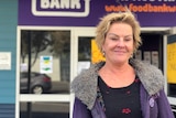 woman with short blonde hair and a grey jacket standing outside of purple bunbury foodbank building 