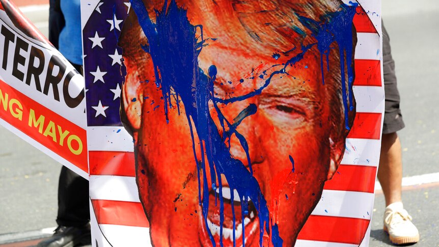 A persona holds placard of Donald Trump's face shouting is superimposed over a circular logo of the US flag splashed in blue.